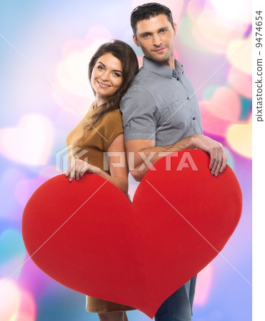 Happy couple in shirt and dress holding handmade paper heart over blurred background 9474654