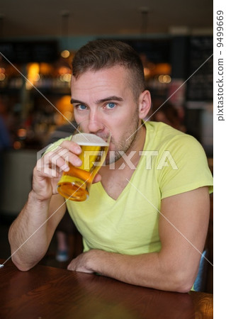 Handsome young man drinking light beer in a pub 9499669