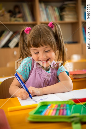 Little schoolgirl sitting behind school desk during lesson in school Little schoolgirl sitting behind school desk during lesson in school 9499923