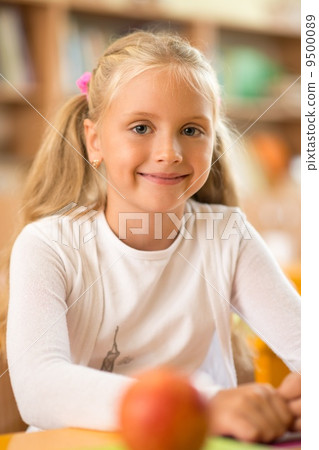 Little schoolgirl sitting behind school desk during lesson in school Little schoolgirl sitting behind school desk during lesson in school 9500089