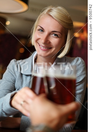 Young woman with beer toasting in a pub 9500742