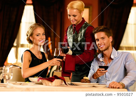 Beautiful young couple in restaurant and waitress with bottle of wine Beautiful young couple in restaurant and waitress with bottle of wine 9501027