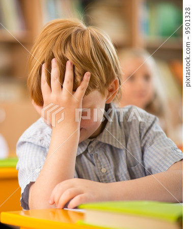 Little redhead schoolboy behind school desk during lesson Little redhead schoolboy behind school desk during lesson 9501328