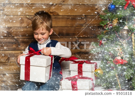 Little boy opening gift box under christmas tree in wooden house interior 9501818