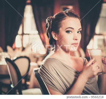 Beautiful young girl with cup of coffee alone in a restaurant 9502218