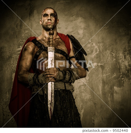 Wounded gladiator holding sword covered in blood with both hands 9502440