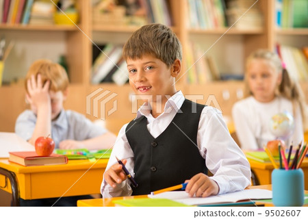 Little schoolboy sitting behind school desk during lesson in school 9502607