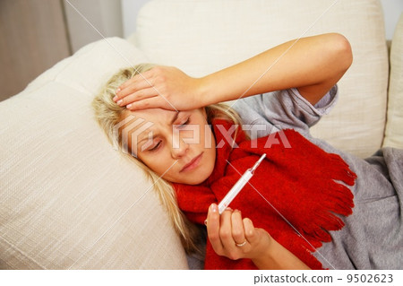 Sick young woman with thermometer lying on sofa at home Sick young woman with thermometer lying on sofa at home 9502623