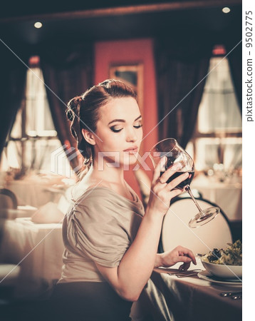 Beautiful young girl with glass of red wine alone in a restaurant 9502775