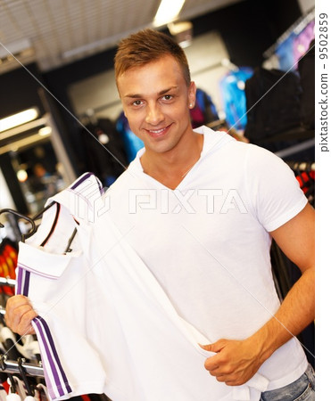 Handsome young man choosing t-shirt in a sport outlet Handsome young man choosing t-shirt in a sport outlet 9502859