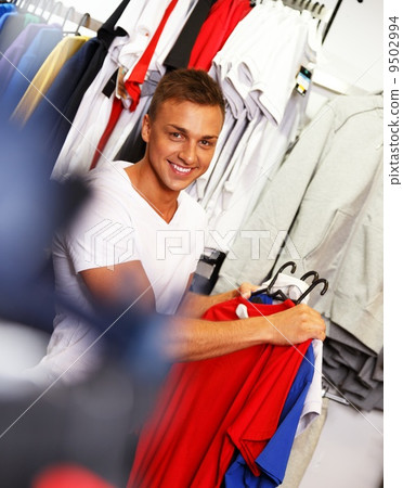 Handsome young man choosing t-shirt in a sport outlet Handsome young man choosing t-shirt in a sport outlet 9502994