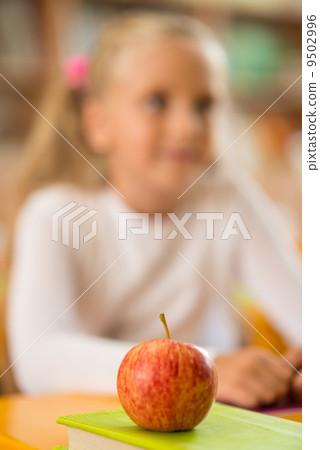 Apple in front of little schoolgirl sitting behind school desk during lesson in school Apple in front of little schoolgirl sitting behind school desk during lesson in school 9502996