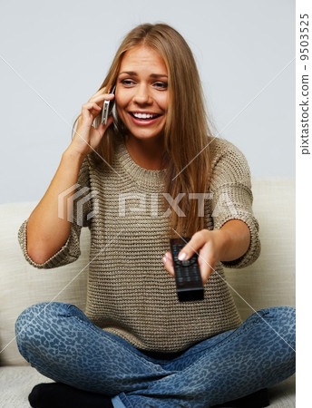 Young beautiful woman on a sofa with remote control and mobile pone 9503525