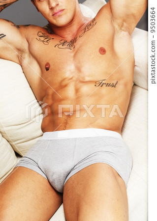 Man with beautiful muscular tattooed torso in underwear lying on sofa 9503664
