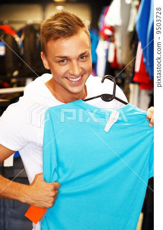 Handsome young man choosing t-shirt in a sport outlet Handsome young man choosing t-shirt in a sport outlet 9503728