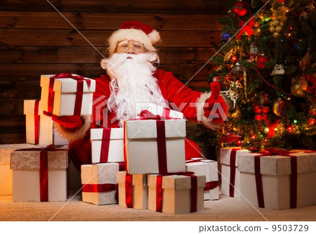 Santa Claus sitting on a carpet in wooden home interior with gift boxes around him Santa Claus sitting on a carpet in wooden home interior with gift boxes around him 9503729