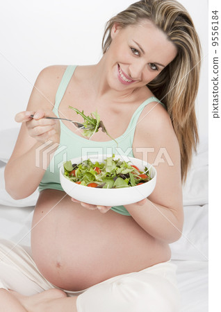 .Pregnant woman in bed eating salad 9556184