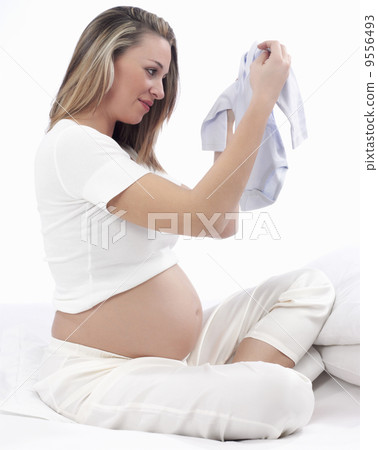 Beautiful Pregnant Young Woman Holding Up New Baby Clothes, Waiting For Her Baby To Be Born Beautiful Pregnant Young Woman Holding Up New Baby Clothes, Waiting For Her Baby To Be Born 9556493