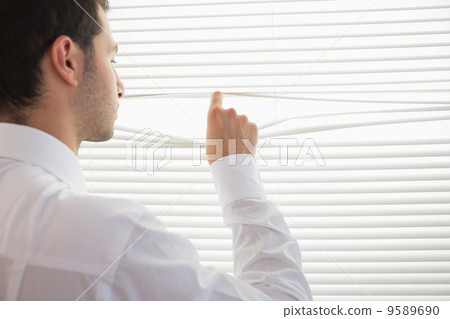 Rear view of handsome businessman spying through roller blind Rear view of handsome businessman spying through roller blind 9589690