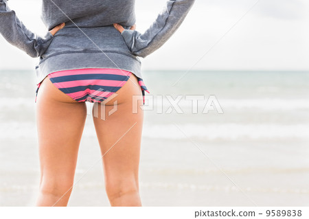 Mid section of a woman in bikini bottom and jacket at beach 9589838