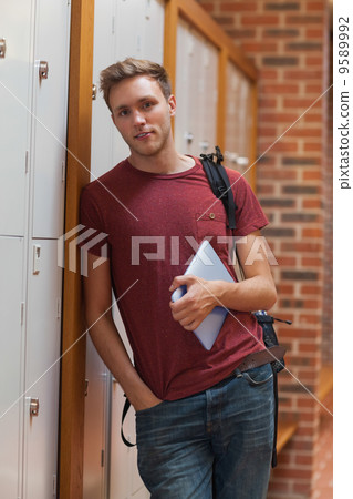 Handsome student leaning against lockers holding tablet Handsome student leaning against lockers holding tablet 9589992