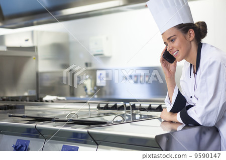Young smiling chef standing next to work surface phoning Young smiling chef standing next to work surface phoning 9590147