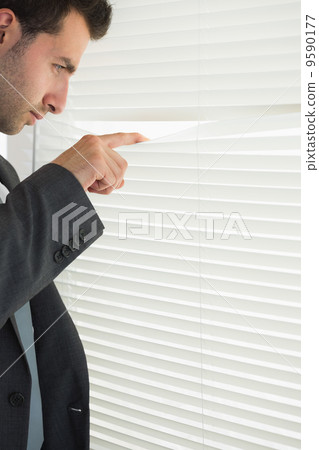 Handsome frowning businessman spying through roller blind 9590177