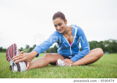 Woman stretching her leg while sitting on the grass 9590474