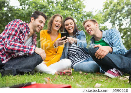 Happy college students looking at mobile phone in park Happy college students looking at mobile phone in park 9590618