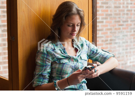 Casual smiling student sitting next to window texting Casual smiling student sitting next to window texting 9591159
