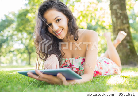 Stylish smiling brunette lying on a lawn using tablet Stylish smiling brunette lying on a lawn using tablet 9591681