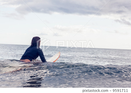 Rear view of a woman sitting on surfboard in water 9591711