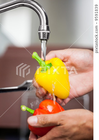 Kitchen porter washing red and yellow pepper under running tap 9591839