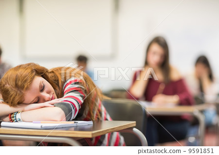 Blurred students in the classroom with one asleep girl 9591851