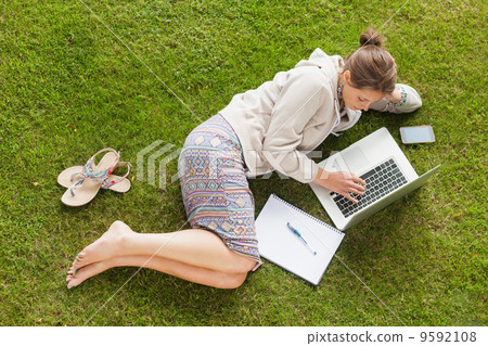 Female student using laptop with books at the park 9592108