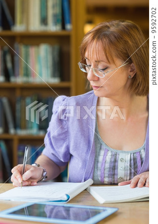 Mature student writing notes at desk in the library 9592702