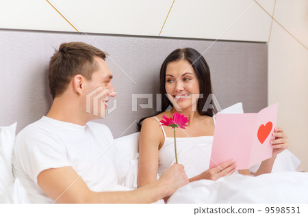 smiling couple in bed with postcard and flower 9598531