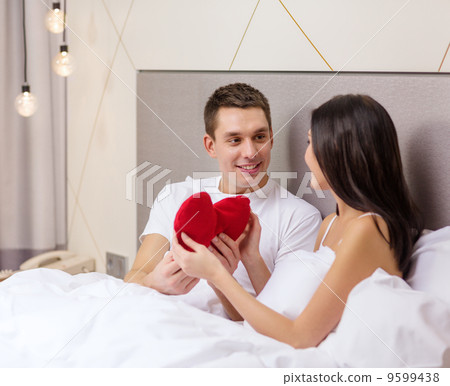 smiling couple in bed with red heart shape pillow smiling couple in bed with red heart shape pillow 9599438