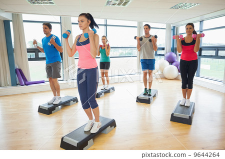 Instructor with fitness class performing step aerobics exercise