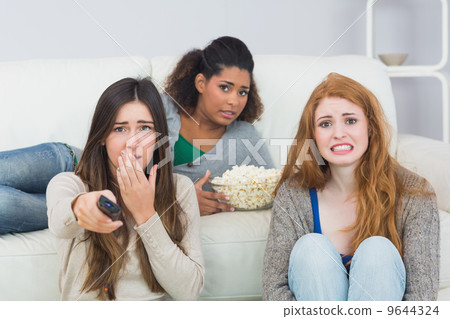 Scared friends with remote control and popcorn bowl at home 9644324