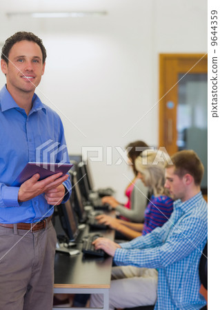 Teacher with students using computers in computer room 9644359