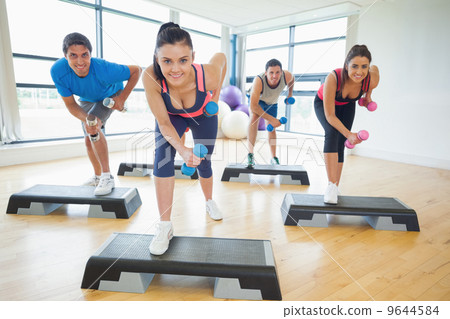 Instructor with fitness class performing step aerobics exercise 9644584