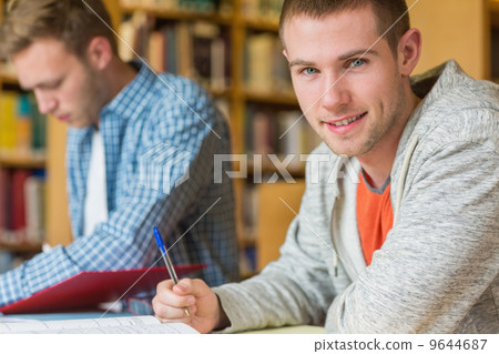 Portrait of a smiling male student at library desk 9644687
