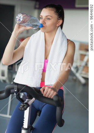 Tired woman drinking water while working out at spinning class Tired woman drinking water while working out at spinning class 9644692