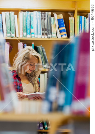 Student reading book amid bookshelves in the library Student reading book amid bookshelves in the library 9644693