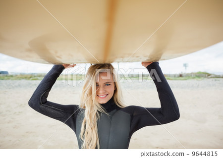 Smiling woman in wet suit holding surfboard over head Smiling woman in wet suit holding surfboard over head 9644815
