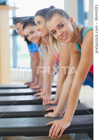 Instructor with fitness class performing step aerobics exercise 9644881