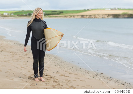 Beautiful woman in wet suit holding surfboard at beach 9644968
