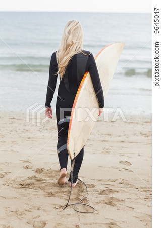 Rear view of a woman in wet suit holding surfboard at beach Rear view of a woman in wet suit holding surfboard at beach 9645047