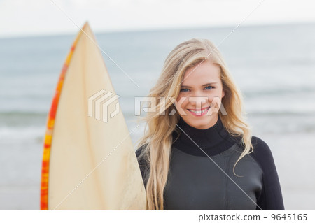 Smiling woman in wet suit holding surfboard at beach 9645165
